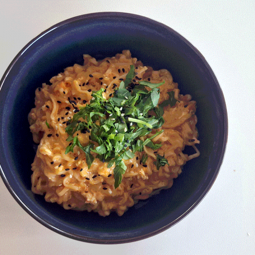 Cremige Käse-Ramen in einer dunklen Schüssel, garniert mit frischen Kräutern und schwarzem Sesam