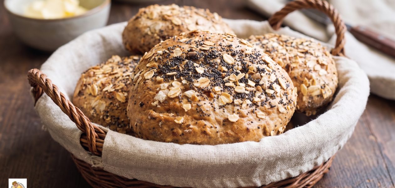 Goldbraun ausgebackene Haferflockenbrötchen mit Mohn und Haferflocken-Topping, serviert in einem geflochtenen Brotkorb mit Leinentuch.
